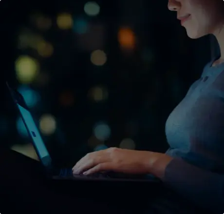A person typing on a laptop in a dimly lit environment, with colorful bokeh lights in the background, suggesting a focused work setting.